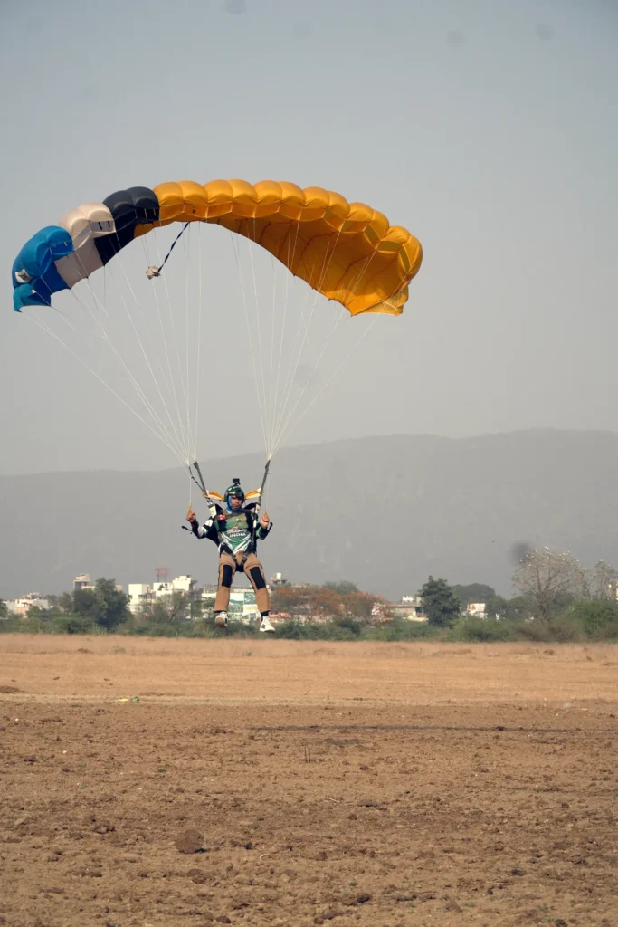 A skydiver on final approach under an orange and blue canopy.